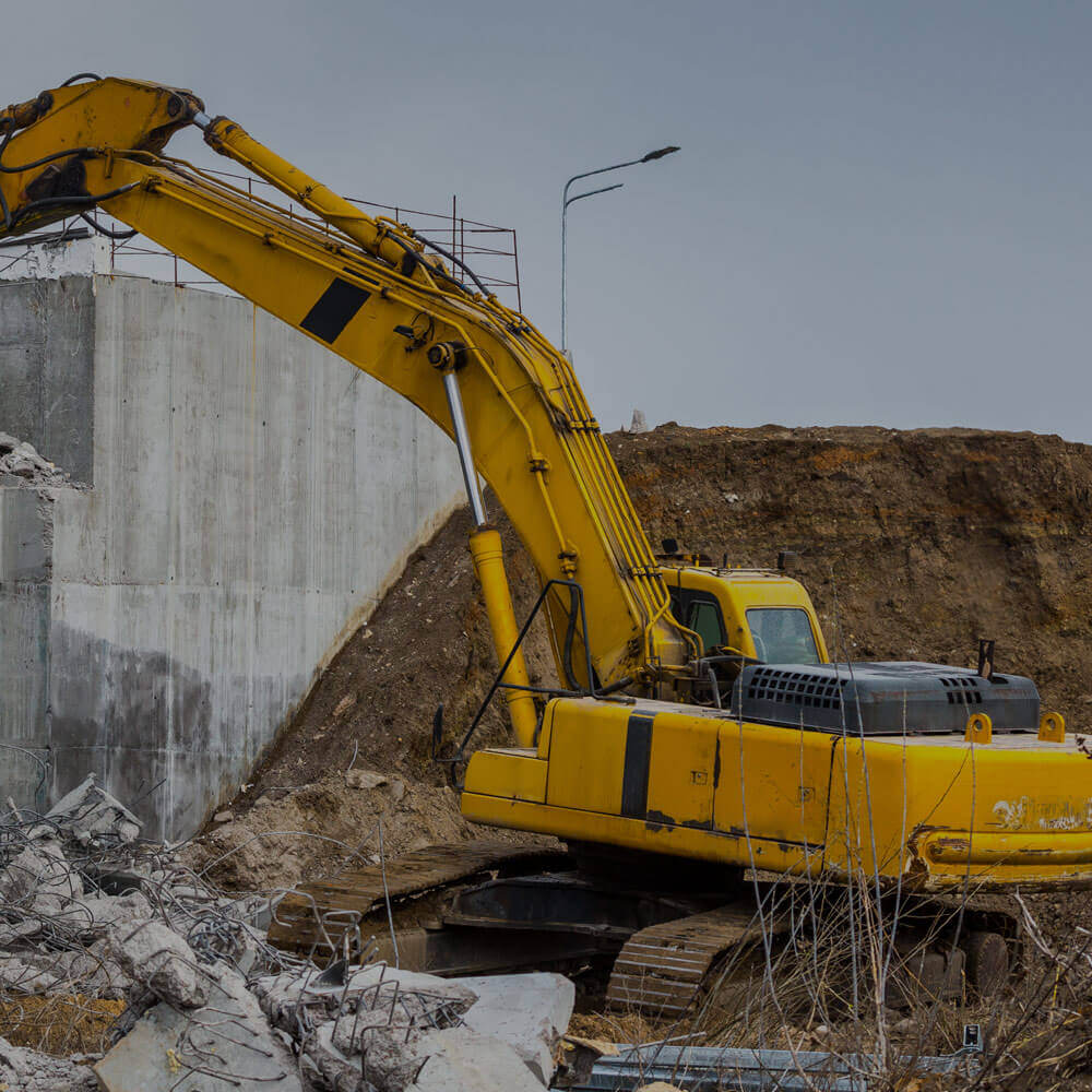 Professional demolition of reinforced concrete structures using industrial hydraulic hammer.